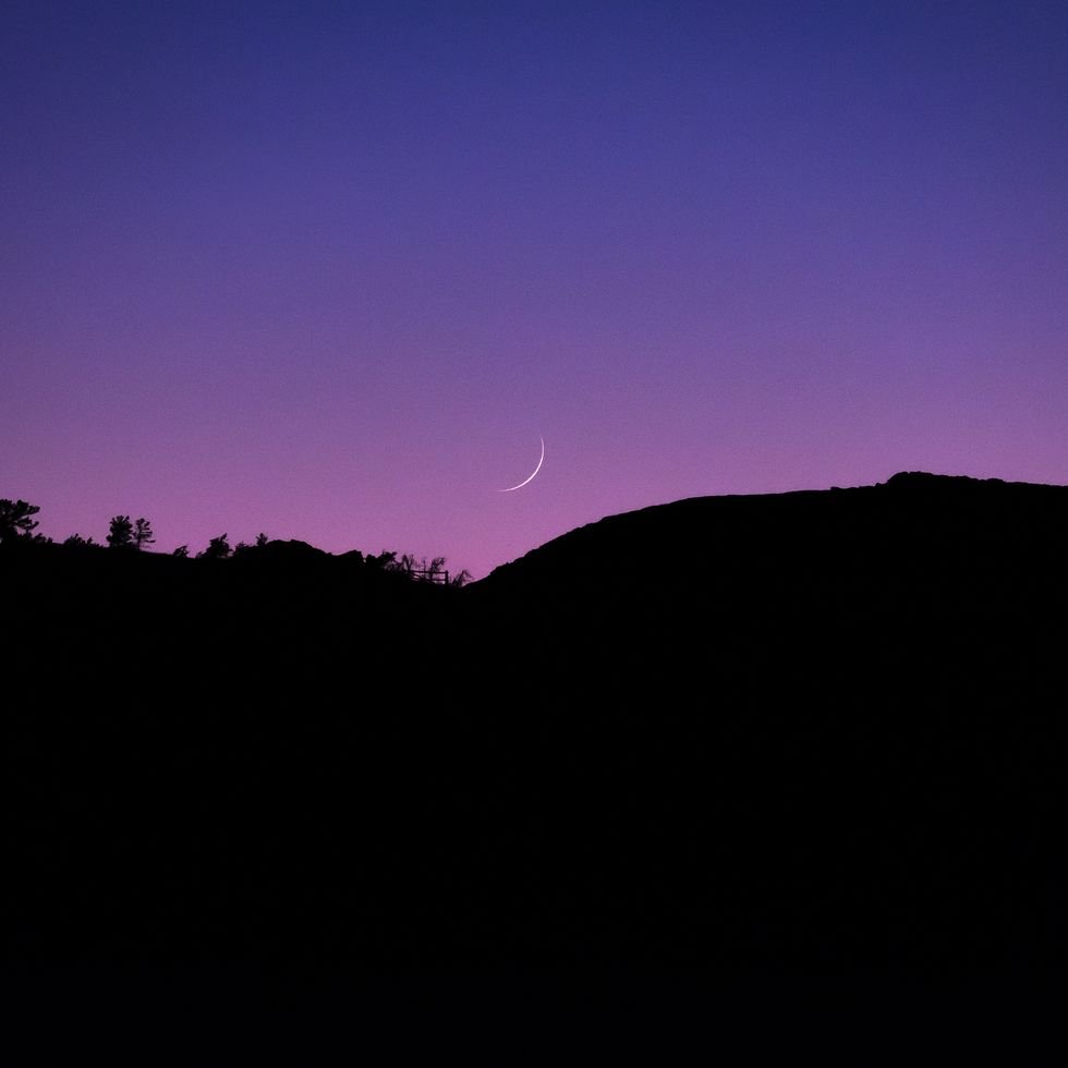a crescent moon descends into a purple sky at craters of the moon, idaho, usa