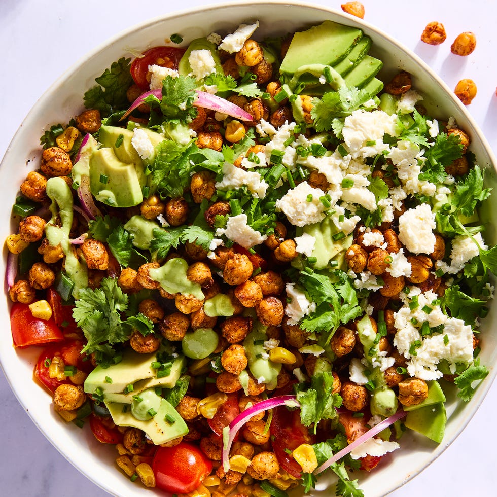 Salad sprinkled with crispy chickpeas, avocado slices, red onions, tomato slices, corn, and topped with herbs and cheese