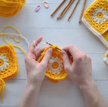 hands making crochet granny squares in yellow and cream yarn