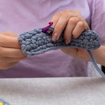 woman's hands working crochet in blue chunky yarn
