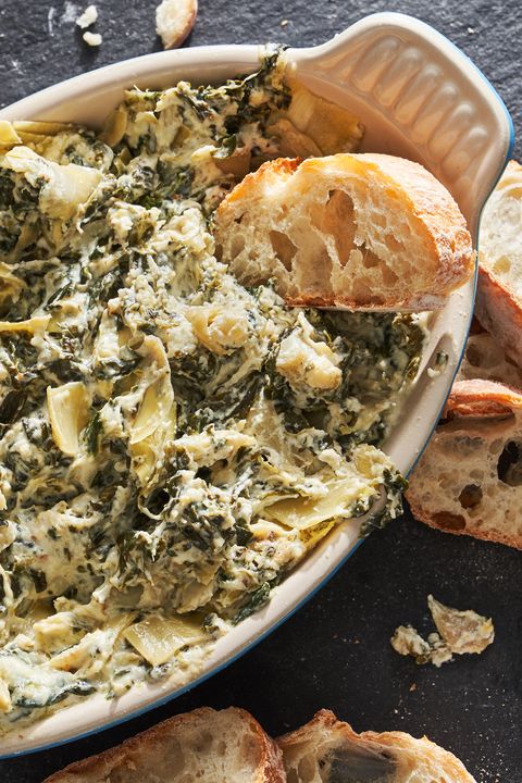 spinach and artichoke dip in a blue dish surrounded by bread slices