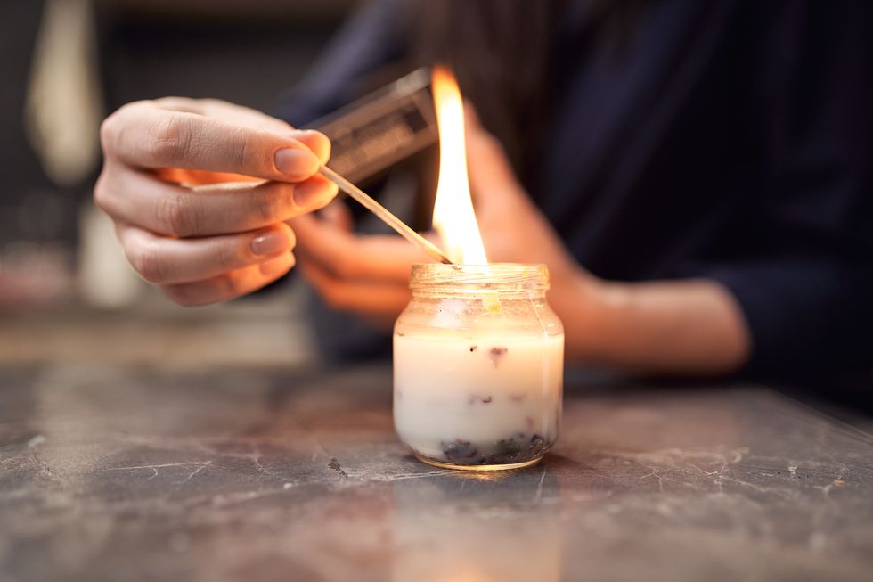 woman lighting fragrant candle placed on table