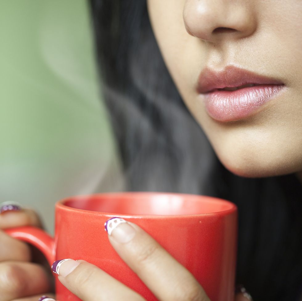 cropped close up of young woman with hot steaming coffee mug