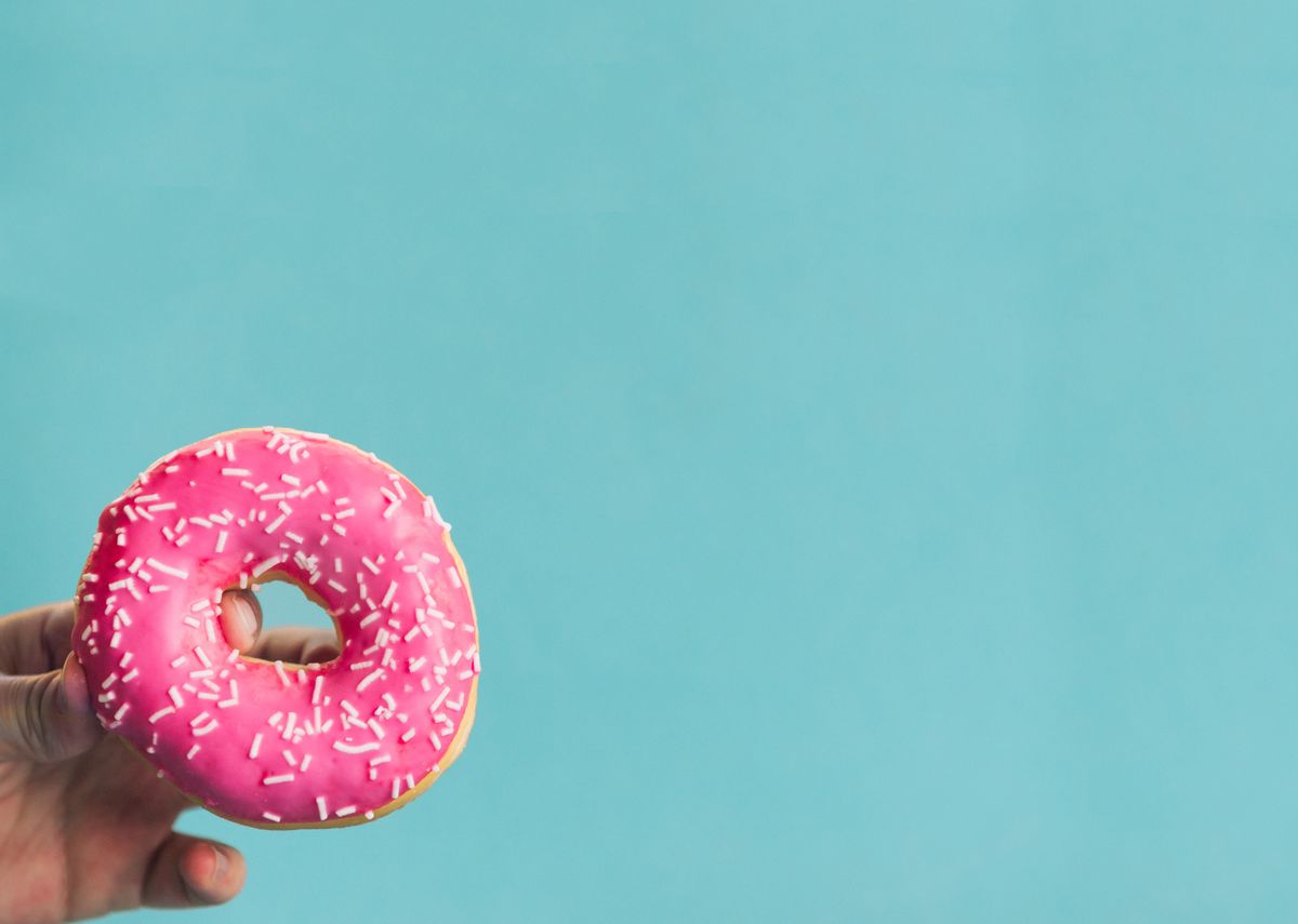 cropped hand holding donut against blue background