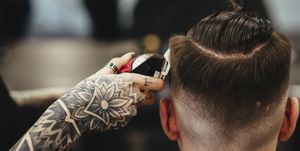 cropped hand of female barber cutting male customer's hair in salon