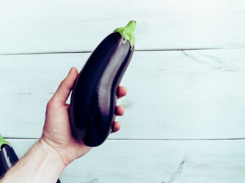 cropped hand of man holding eggplant over table
