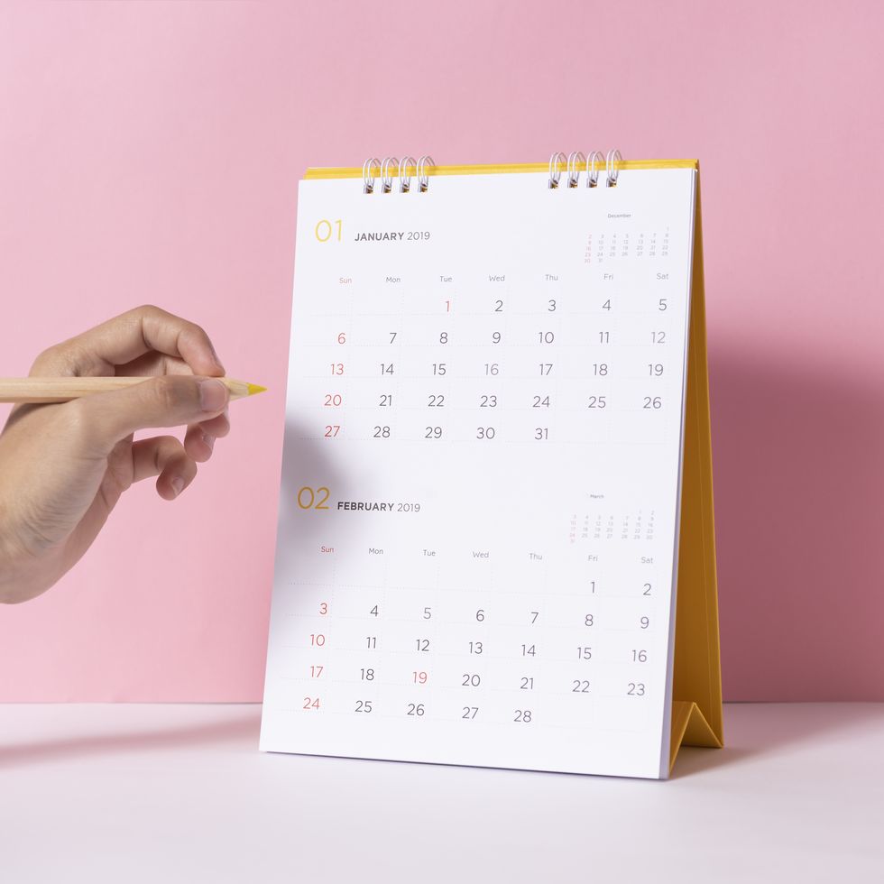 cropped hand of person holding colored pencil by calendar on table