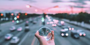 Cropped Hand Of Person Holding Crystal Ball Against Road During Sunset