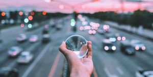 Cropped Hand Of Person Holding Crystal Ball Against Road During Sunset