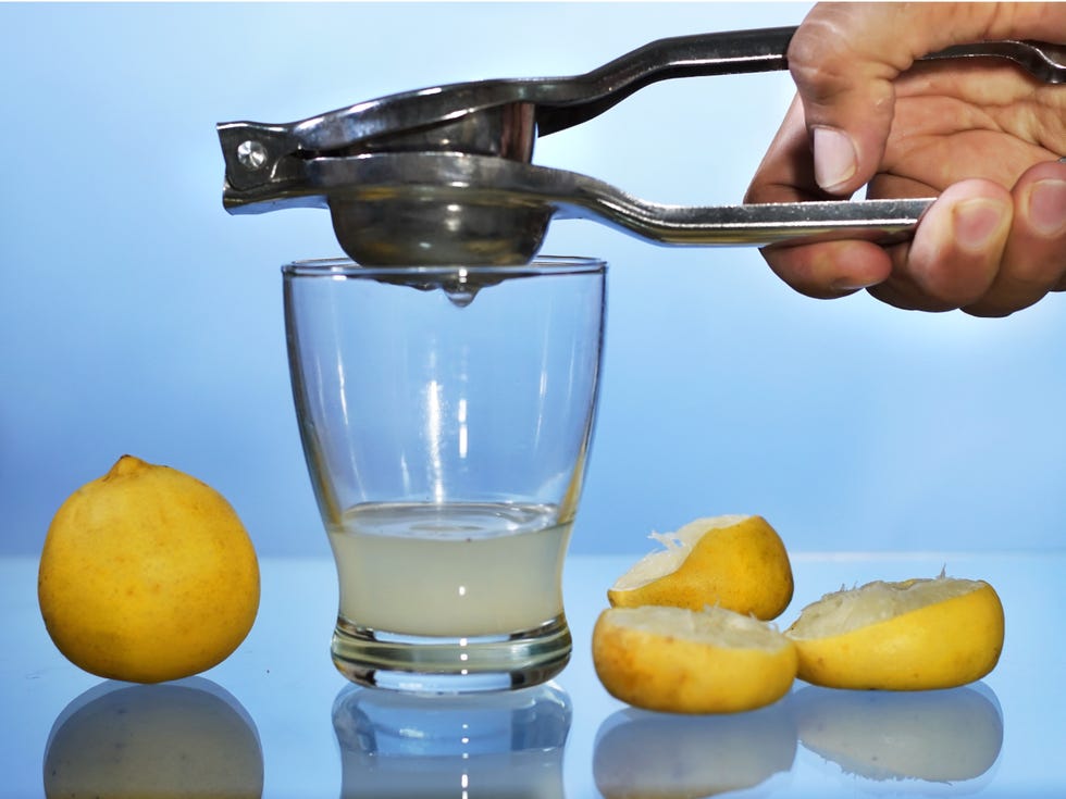 cropped hand of person preparing drink in glass by lemons