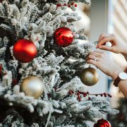 cropped hand of woman decorating and hanging baubles on christmas tree