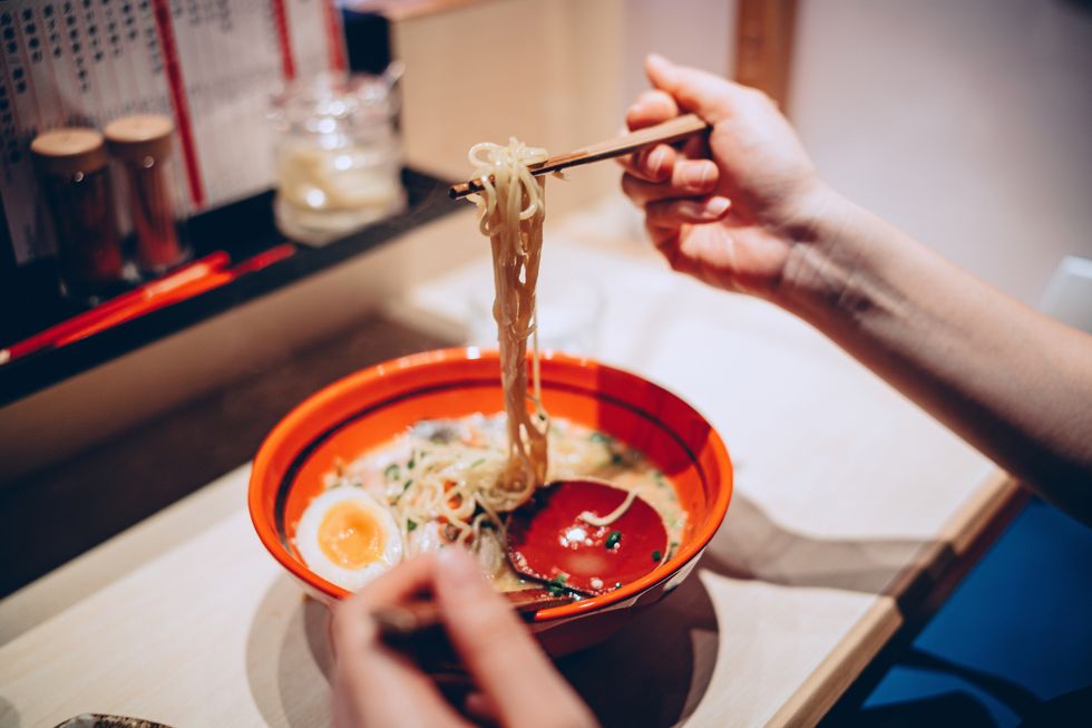 Cropped hand of woman eating a bowl of freshly served traditional Japanese ramen with chopsticks in a Japanese restaurant. Asian cuisine and food culture. Eating out lifestyle
