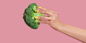 cropped hand of woman holding broccoli against pink background,kyiv,ukraine