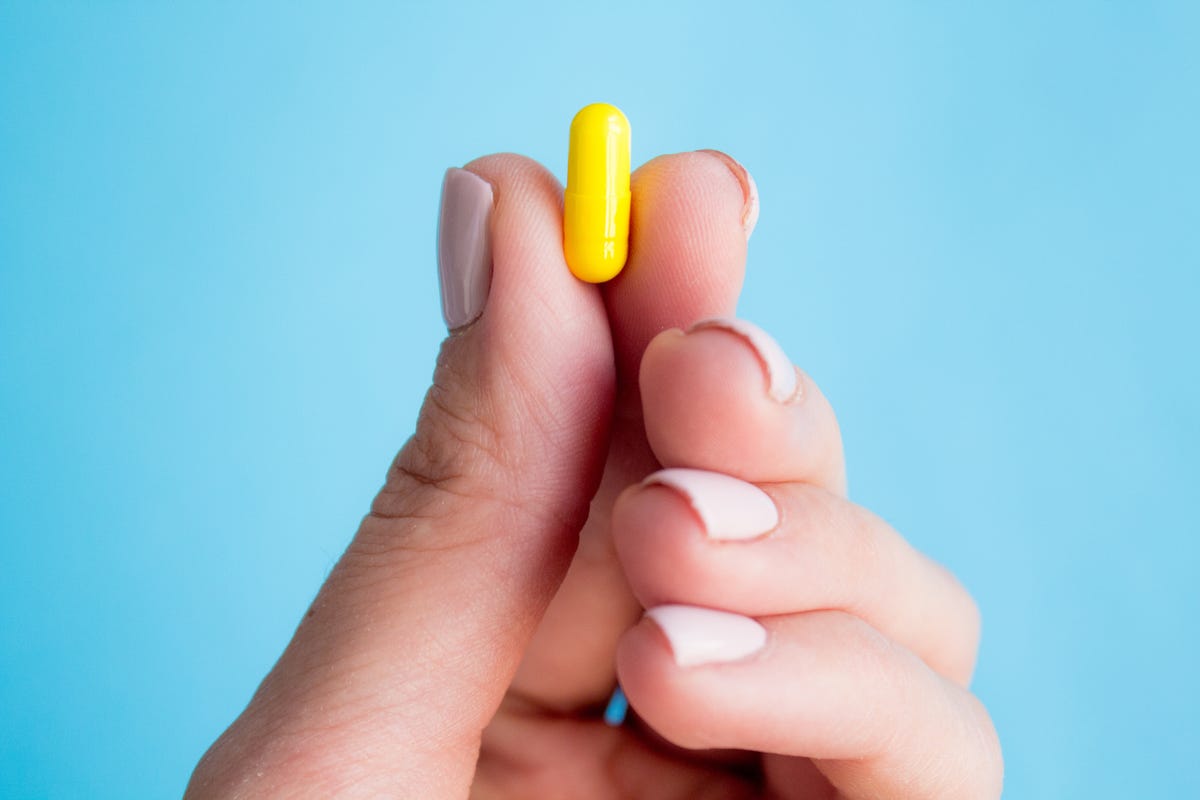 cropped hand of woman holding capsule against blue background