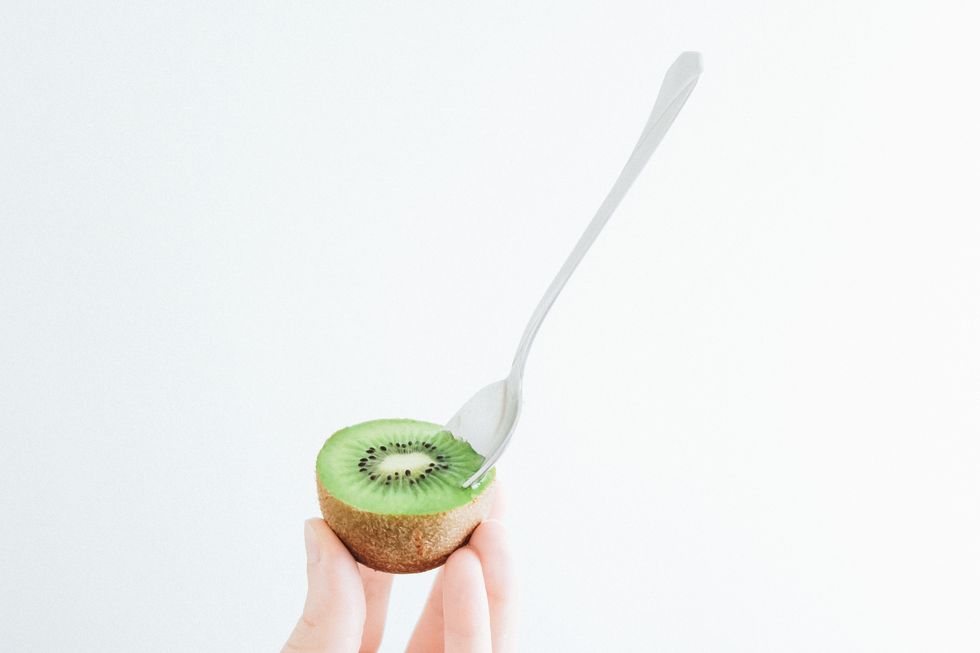 cropped hand of woman holding kiwi against white background