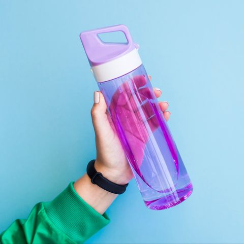 cropped hand of woman holding purple water bottle against blue background