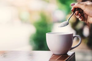 cropped hand of woman holding spoon with sugar over coffee cup on table