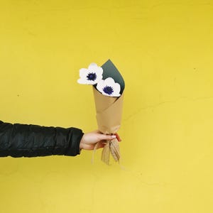 Cropped Hand Of Woman Holding Wrapped Flowers Against Yellow Wall