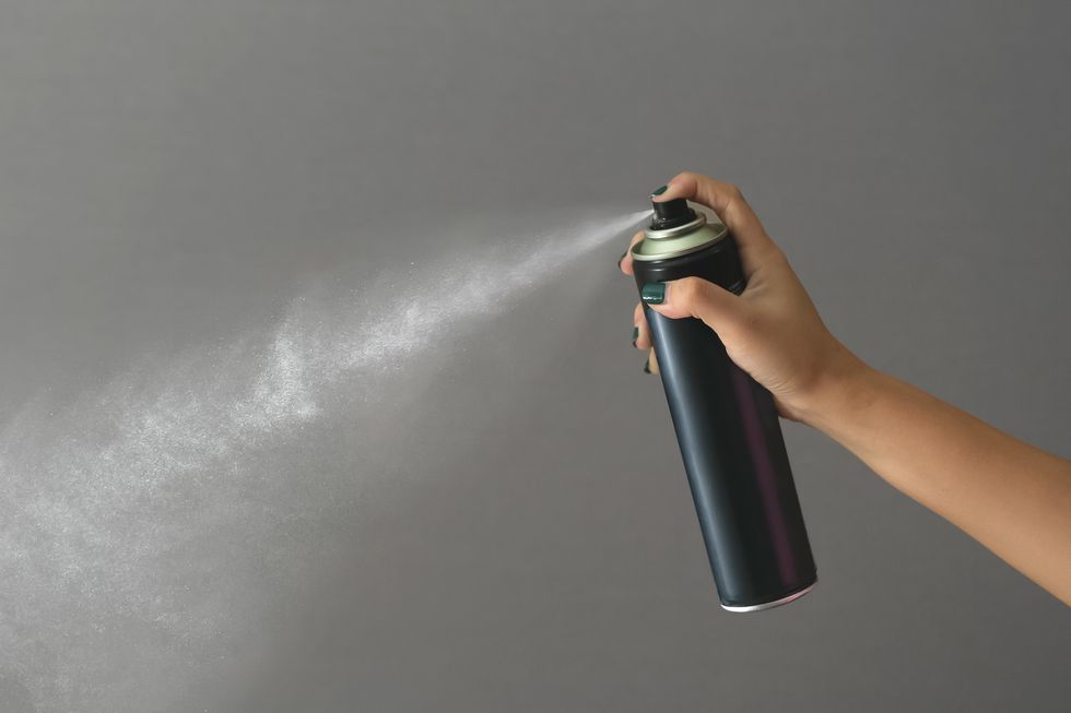 cropped hand of woman spraying against gray background