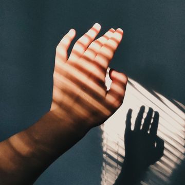 cropped hand of woman with shadow against wall