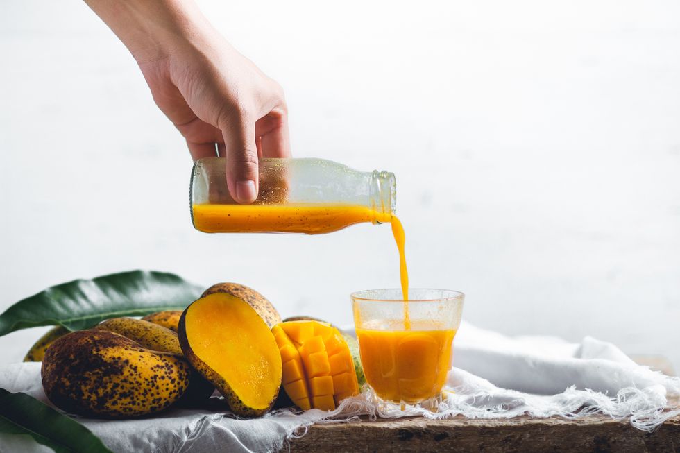 cropped hand pouring mango juice from bottle in glass against white background