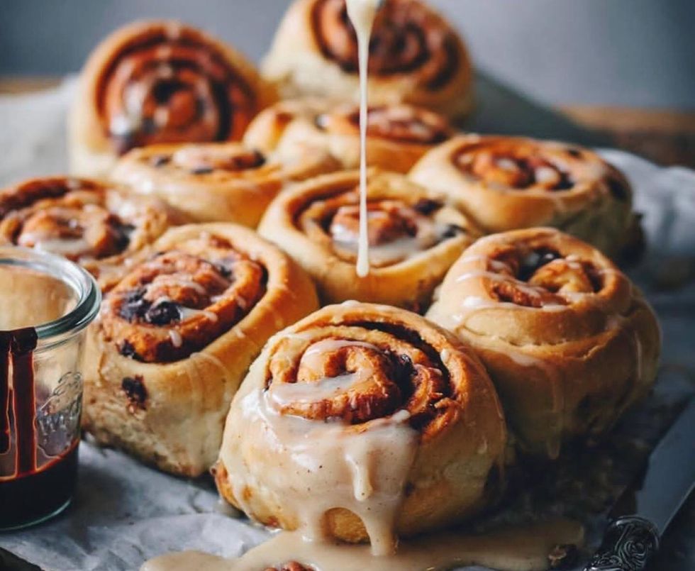 cropped hand pouring syrup on cinnamon rolls