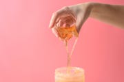 cropped hand pouring water from bottle against pink background