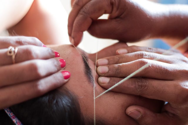 cropped hands of beautician threading woman eyebrows