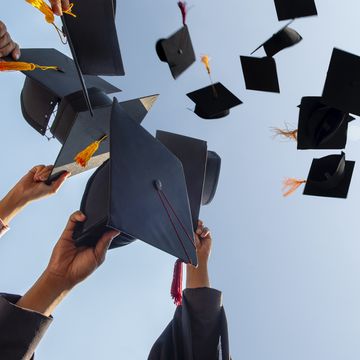 cropped hands of people throwing mortarboards against clear sky