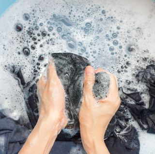 two hands scrubbing dark garment in soapy water