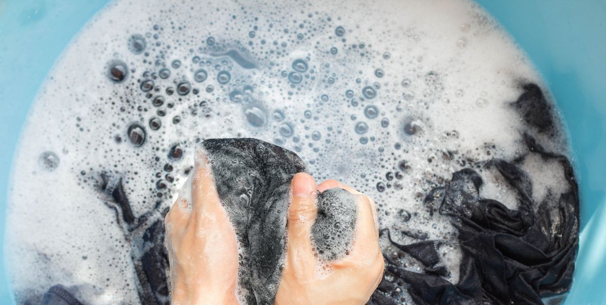 two hands scrubbing dark garment in soapy water