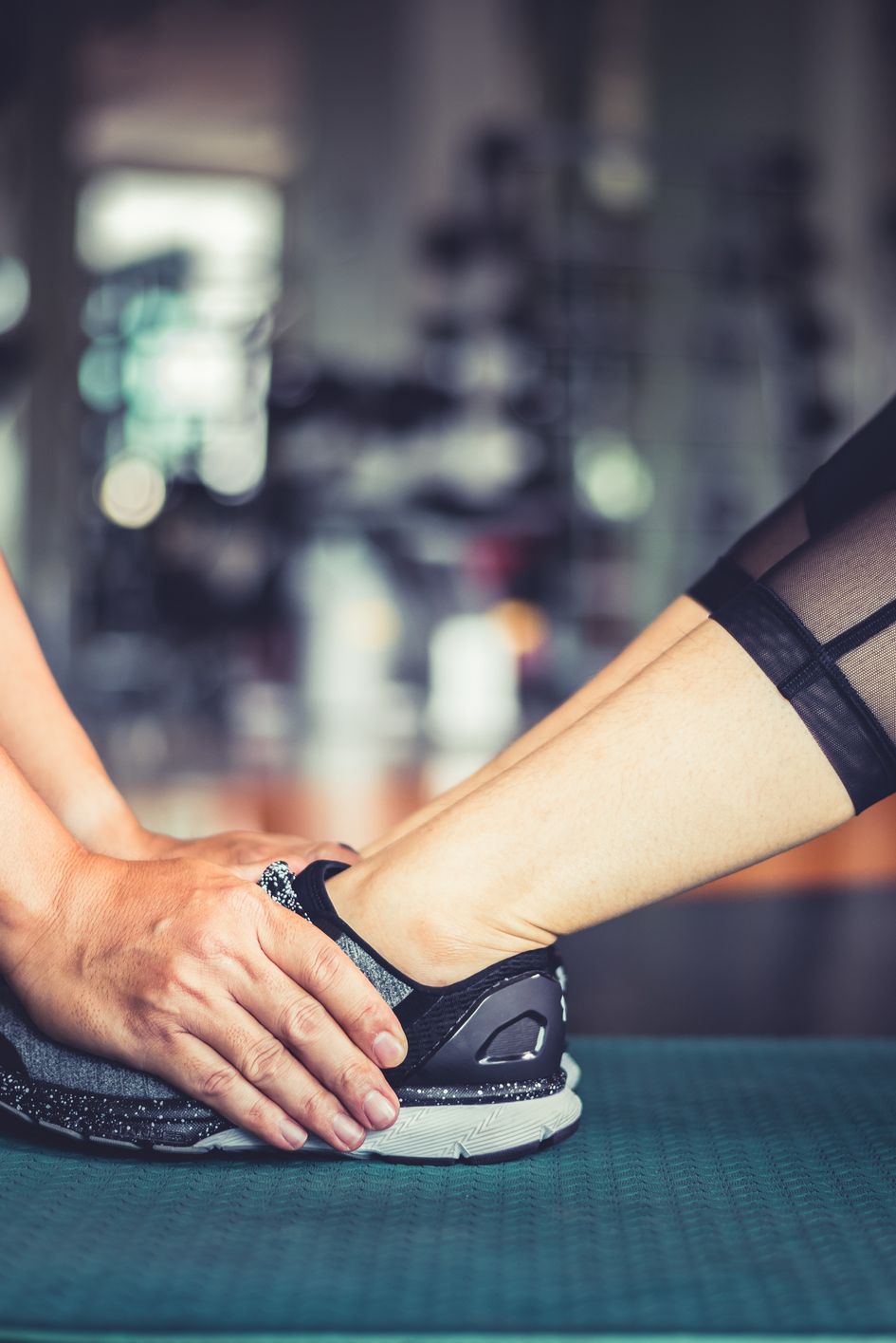 Cropped Hands Of Trainer Holding Woman Leg During Exercise In Gym