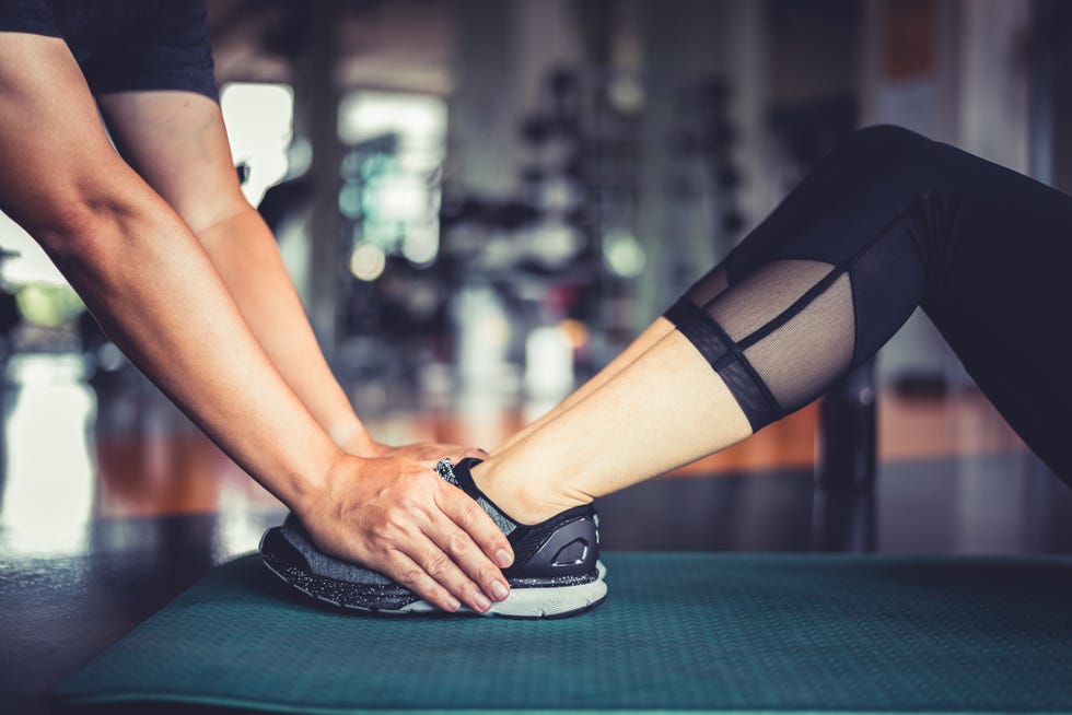 Cropped Hands Of Trainer Holding Woman Leg During Exercise In Gym