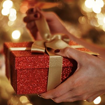 cropped hands of woman opening gift box against christmas lights