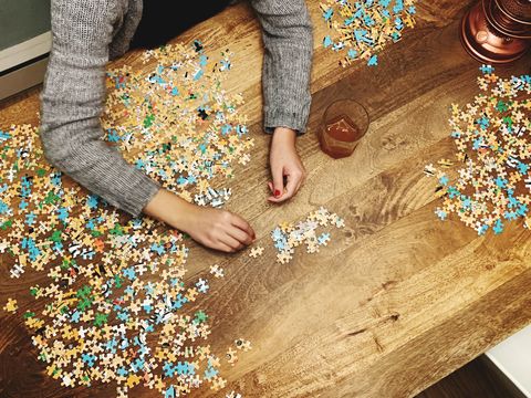 cropped hands of woman playing jigsaw puzzle on wooden table at home