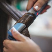 cropped image of beautician straightening hair of customer