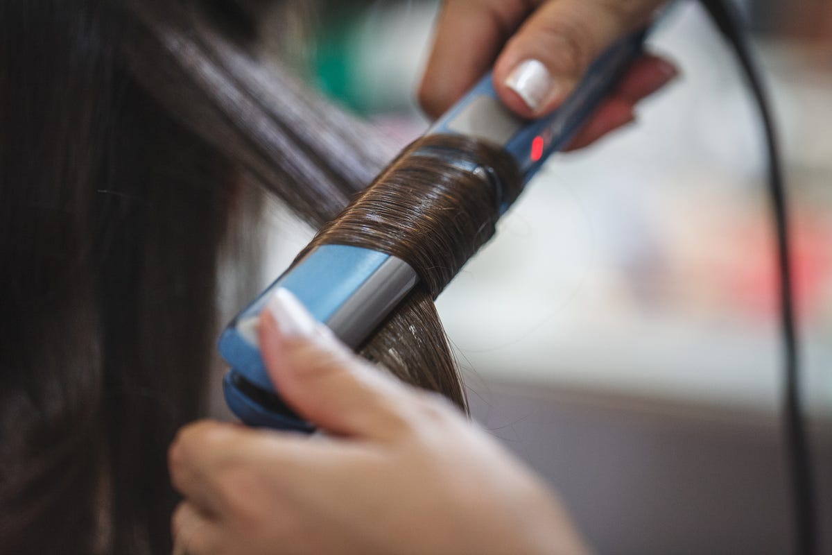 cropped image of beautician straightening hair of customer