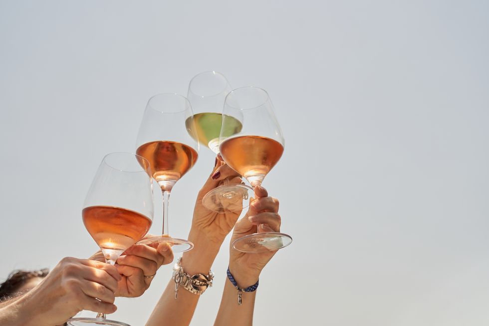cropped image of friends cheering with wine in celebration against blue sky food and drink concept