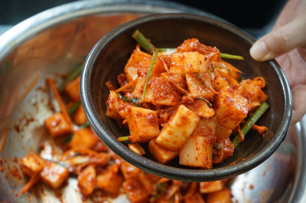 cropped image of hand holding kimchee in bowl over cooking pan