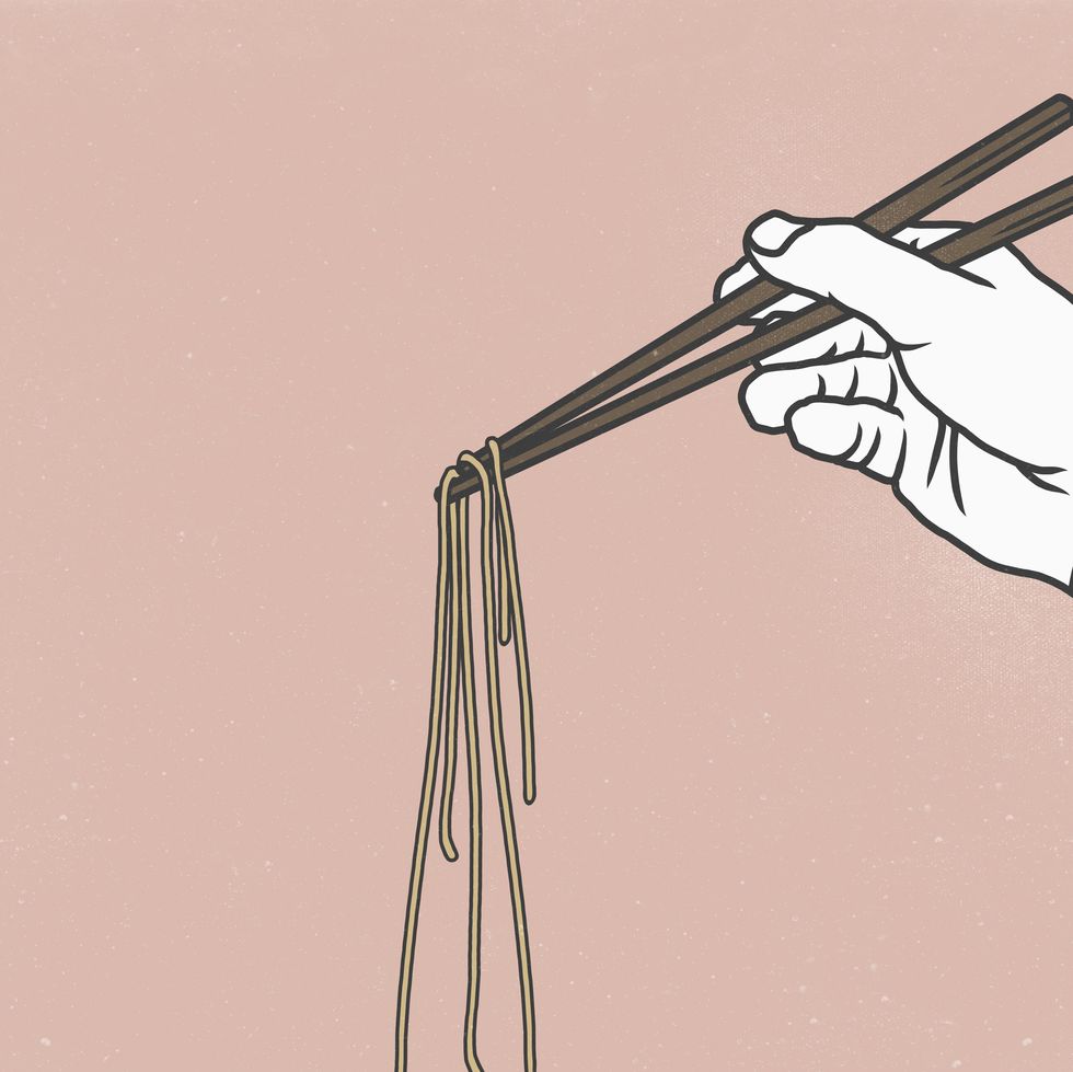 Cropped image of hand holding noodles with chopsticks against pink background