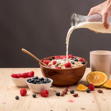 Cropped Image Of Hand Pouring Milk In Oatmeal On Table Against Gray Background