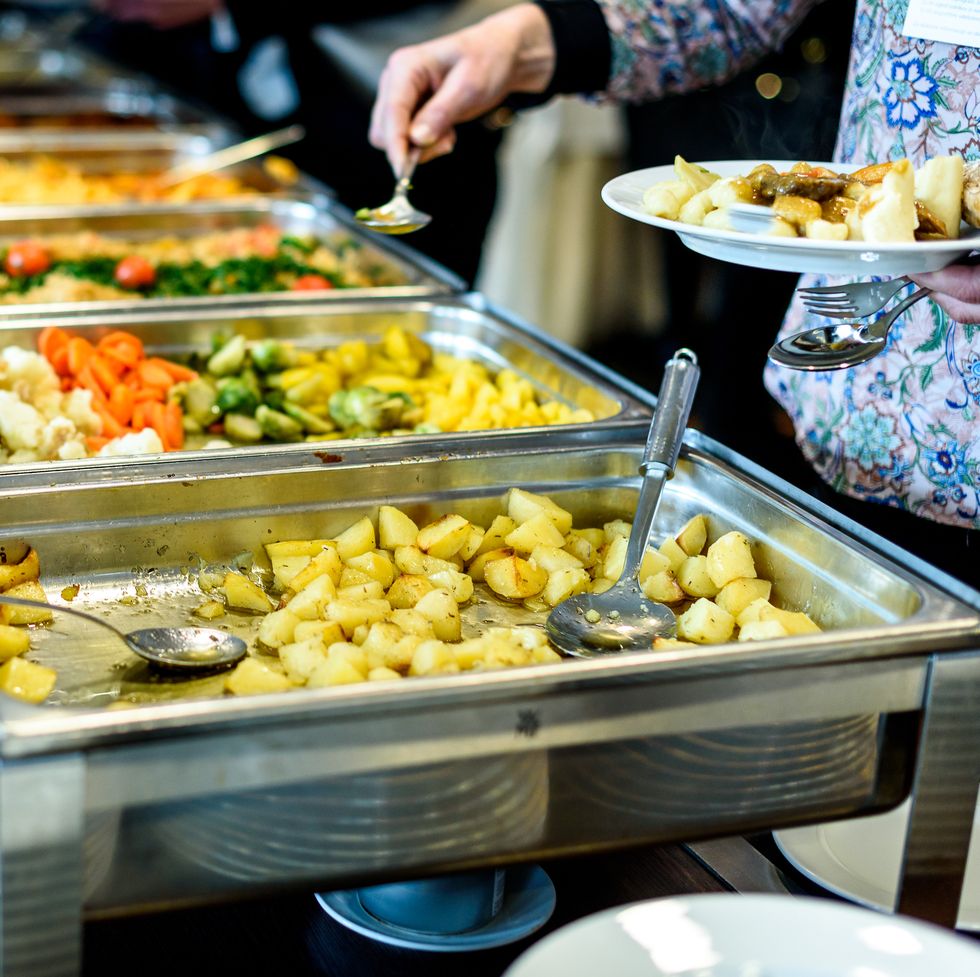 person filling a plate with food from a buffet