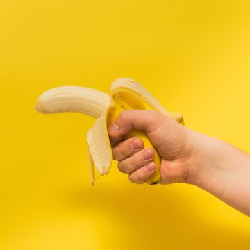 cropped image of person holding peeled banana against yellow background