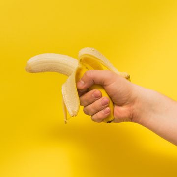 cropped image of person holding peeled banana against yellow background