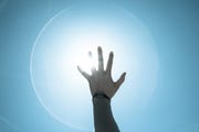 cropped image of person reaching towards bright sun