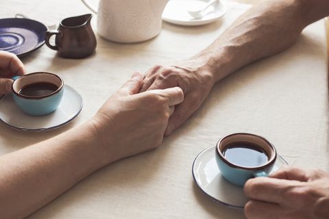 Cropped image of senior couple holding hands and drinking coffee