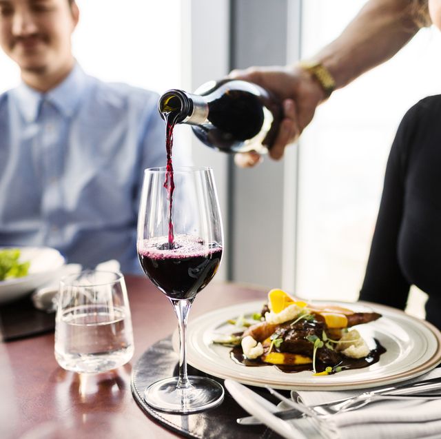 cropped image of waiter serving red wine for female customer at restaurant