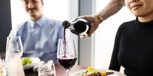 cropped image of waiter serving red wine for female customer at restaurant