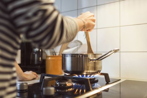 Cropped image of woman holding spatula in sauce pan while cooking food on stove