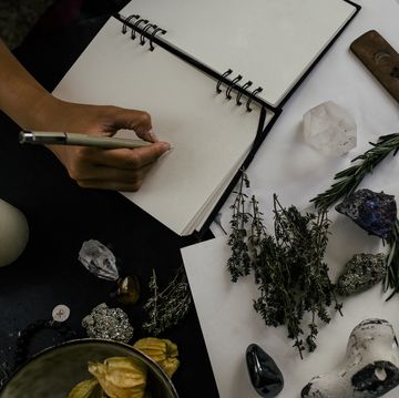 cropped image of woman writing in book by herbs and crystals on table